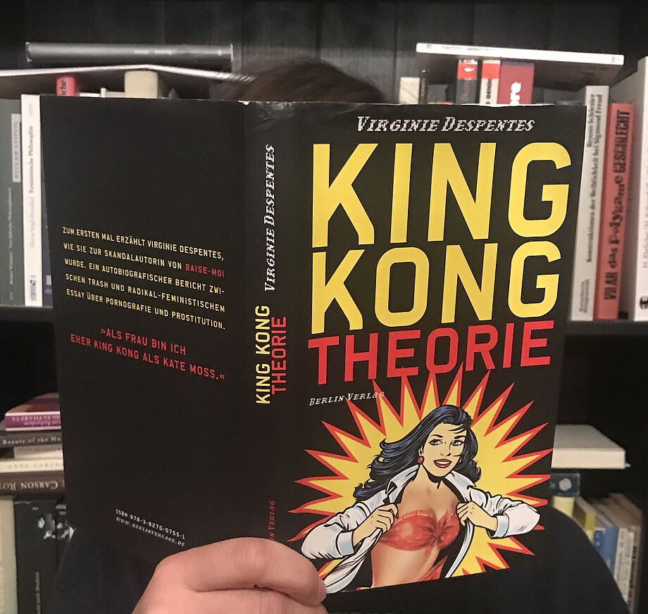 Katharina Kaps mit Buch vor dem Gesicht, auf dem Buchcover zu lesen: Virginie Despentes, King Kong Theorie