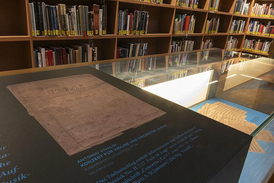 Nahaufnahme eines Elements der Ausstellung in der Bibliothek. Eine alte Schrift auf schwarzem Hintergrund und einem blauen Text darunter.