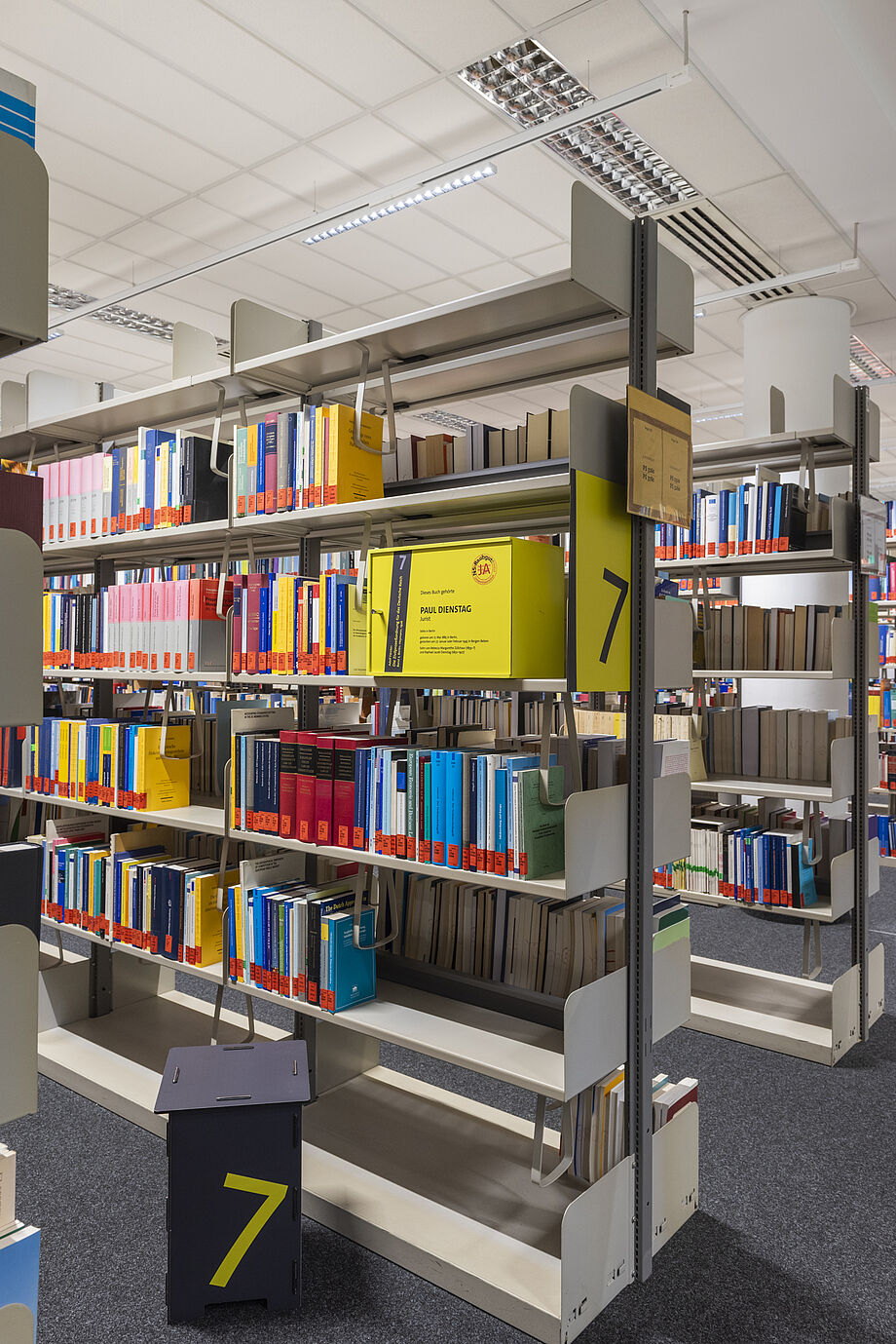 In der Bibliothek mehrere Bücherregale. In einem steht eine der Gelben Infoboxen mit Inhalten zur Ausstellung. 