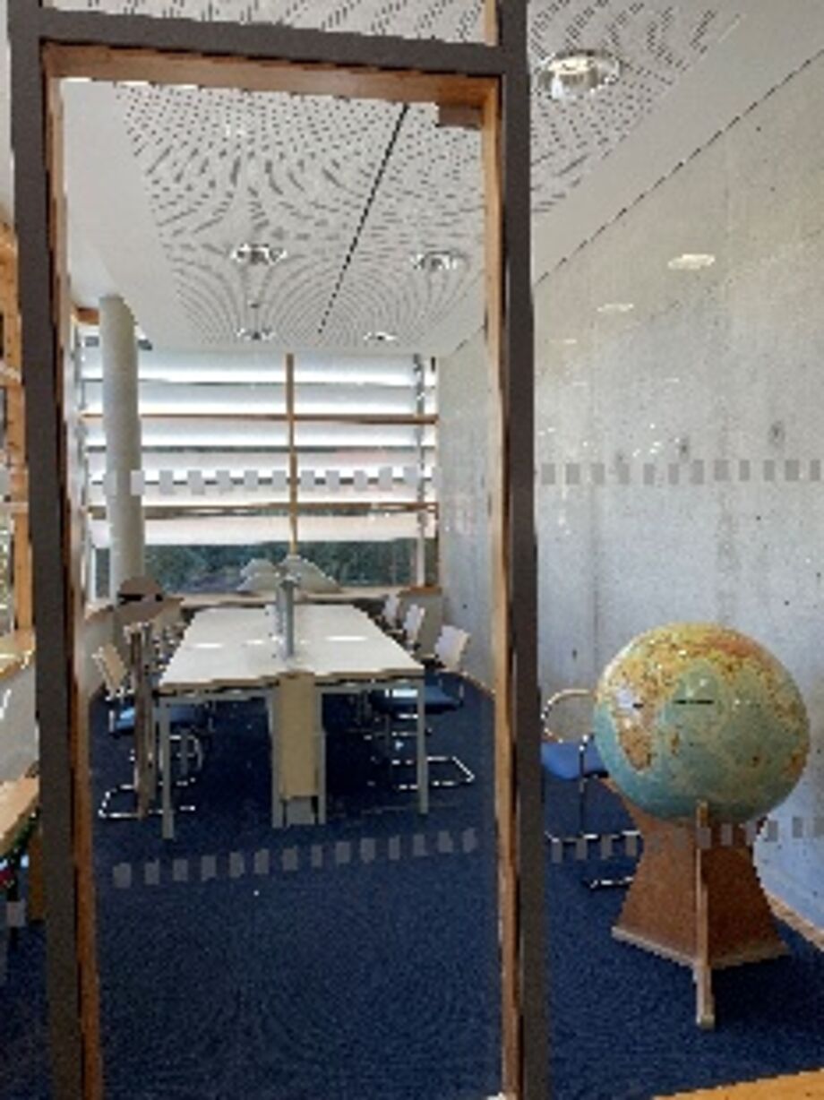 Blick durch die Glastür in den Leseraum in Tharandt. ein Globus steht rechts neben dem Eingang. Der Raum ist mit einem langen weißen Tisch ausgestattet. 